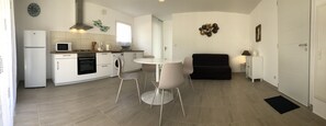 A compact kitchen with a refrigerator, microwave, stove, and washing machine. There is a dining table with chairs and a black sofa.