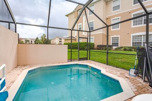 A swimming pool with a glass enclosure, surrounded by a brick patio and a grassy area.