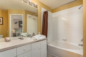 A bathroom with a bathtub, a sink with a mirror, and a shower curtain.