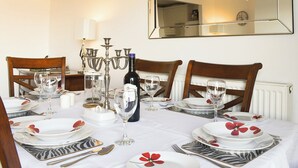 Una mesa de comedor lista con platos, vasos y cubiertos, rodeada de sillas.