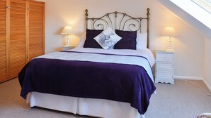 Un dormitorio con cama, dos mesitas de noche con lámparas, un armario de madera y un techo inclinado con tragaluz.