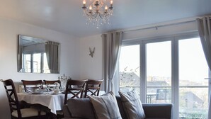 Un comedor con una mesa preparada para cuatro personas, un candelabro y vistas al exterior a través de amplios ventanales.