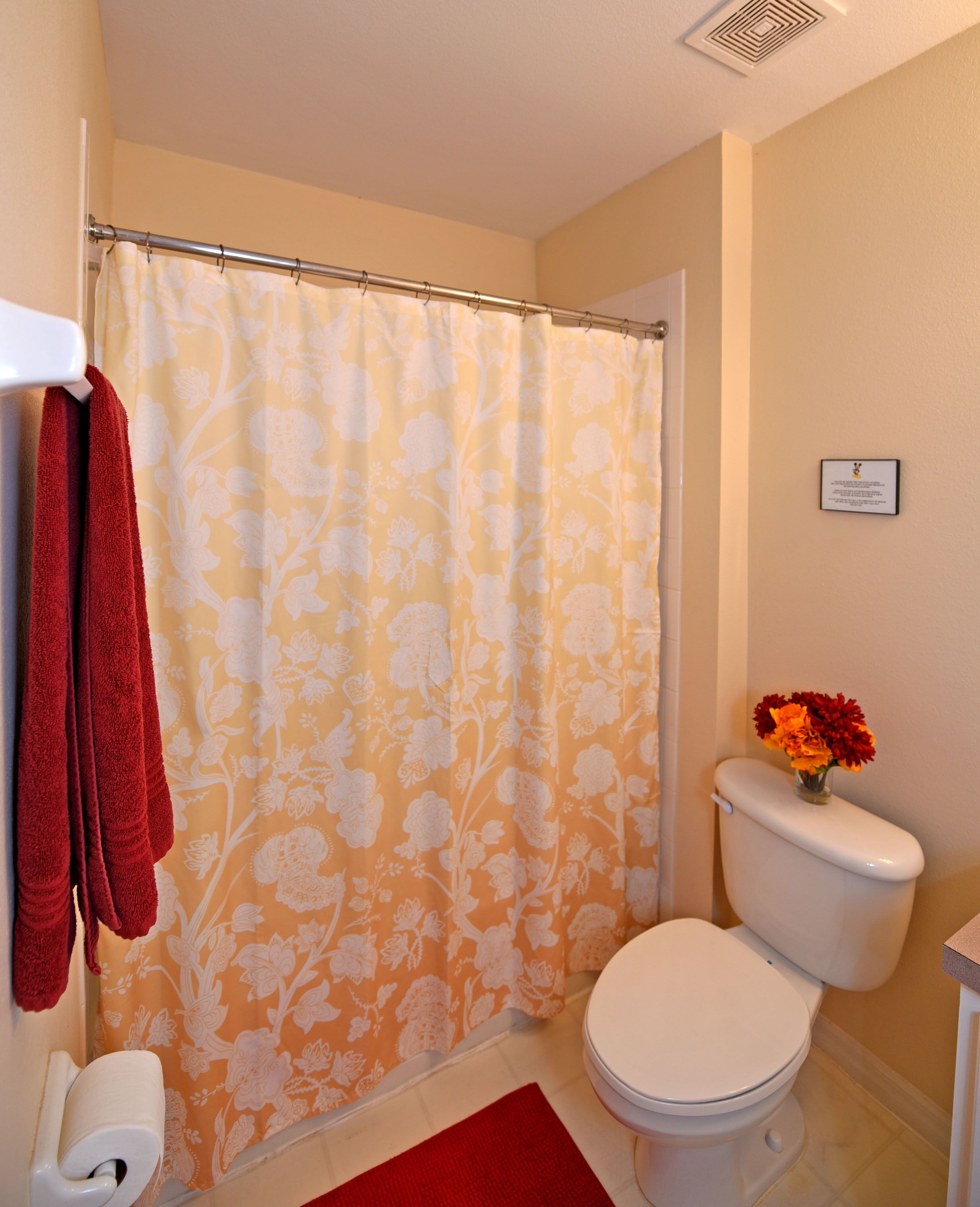 A bathroom with a shower curtain, a toilet, a red towel, and a flower vase.