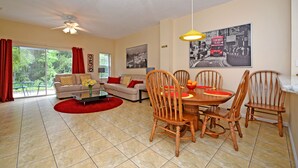 A living room with a sofa, dining table, chairs, and a ceiling fan.