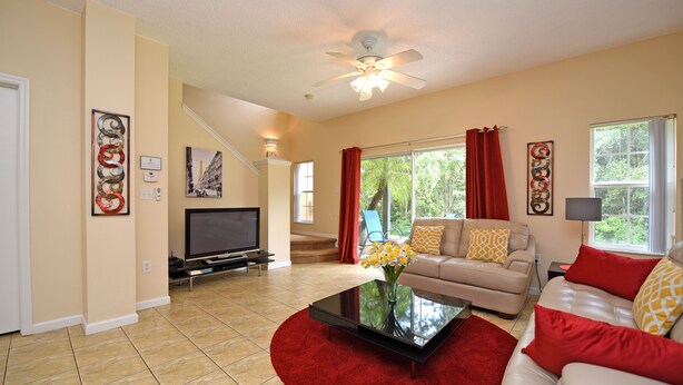 A living room with a flat-screen TV, a sofa, a coffee table, and a ceiling fan.