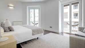 Une chambre moderne avec un grand lit, une table de chevet, une lampe, un tapis à motifs et une vue sur le balcon extérieur.