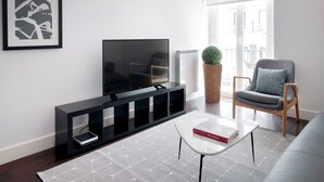 Un salon moderne avec un téléviseur à écran plat posé sur un meuble noir, un fauteuil gris, une table basse blanche et un tapis à motifs.