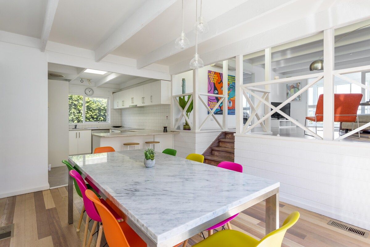 A modern kitchen with white cabinets, a marble island, and colorful chairs.