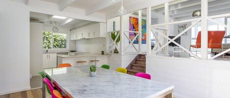 A modern kitchen with white cabinets, a marble island, and colorful chairs.