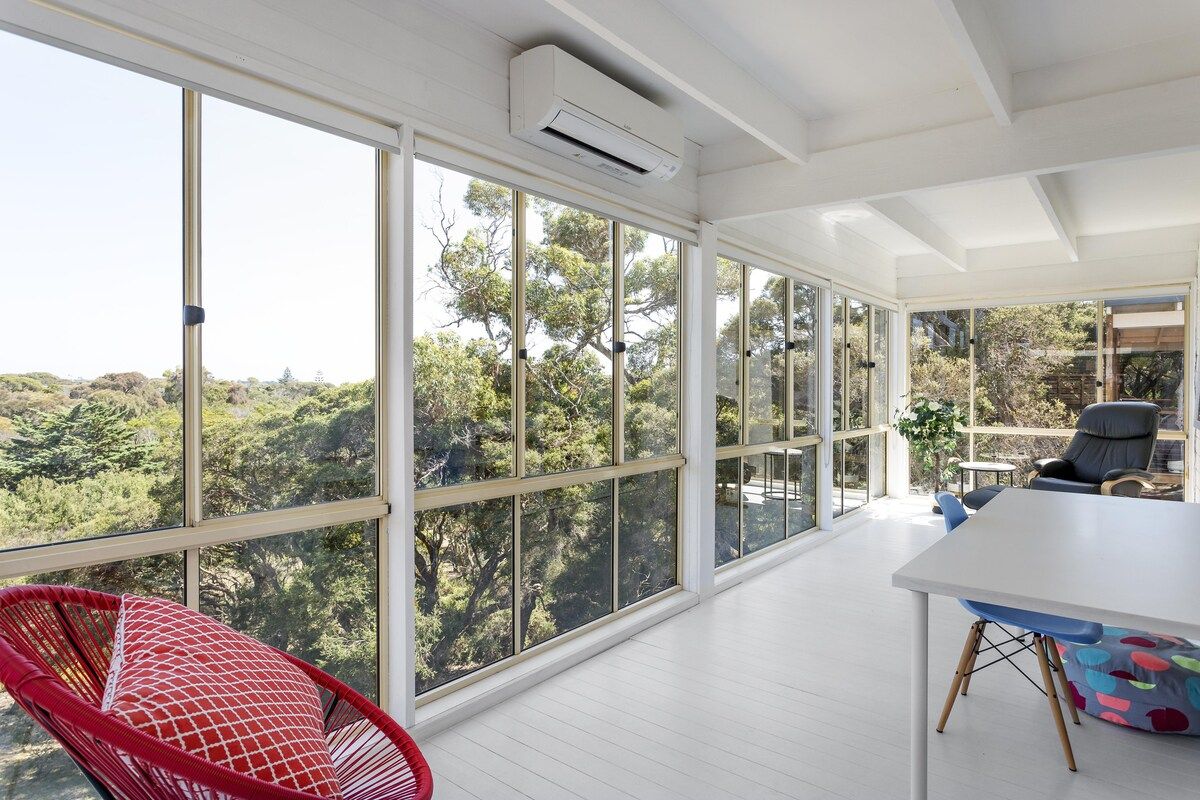 A room with large windows, a white ceiling, and a table with chairs.