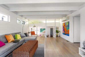 A modern living room with a grey sectional sofa, colorful cushions, a patterned ottoman, a wooden floor, and a large abstract painting on the wall. - At Agnes Ave, Blairgowrie (Blairgowrie)