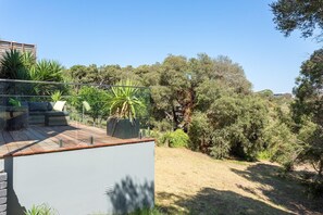 A rooftop terrace with outdoor seating, a large potted plant, and a view of a wooded area.