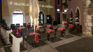 An outdoor café area with tables and chairs, some covered by umbrellas. - Apartment del Pescatore In Downtown (Torri del Benaco)