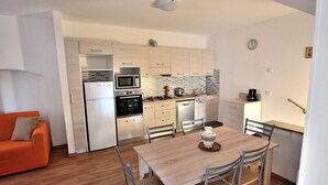 A compact kitchen with modern appliances, a dining area with a wooden table and chairs, and a small orange sofa. - Apartment del Pescatore In Downtown (Torri del Benaco)