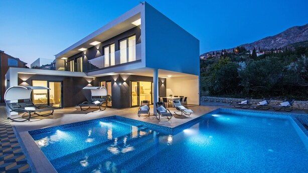 Een modern huis met twee verdiepingen, een zwembad, terras en uitzicht op de bergen.