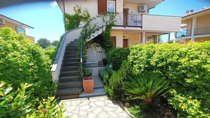 A staircase leading to a building with a balcony, surrounded by lush greenery and potted plants.