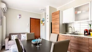 A modern living room with a dining table, sofa, and kitchen area with cabinets and a coffee machine.