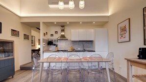 A modern kitchen with white cabinets, a stainless steel range hood, and a dining area with a wooden table and clear chairs. - Great View San Marco - historic center of Florence (Firenze)