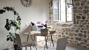 A room with a wooden ceiling, stone walls, a wooden table with chairs, a potted plant, a clock, and a window with a view. - B&B Au Chant De L'eau (Siaugues-Sainte-Marie)