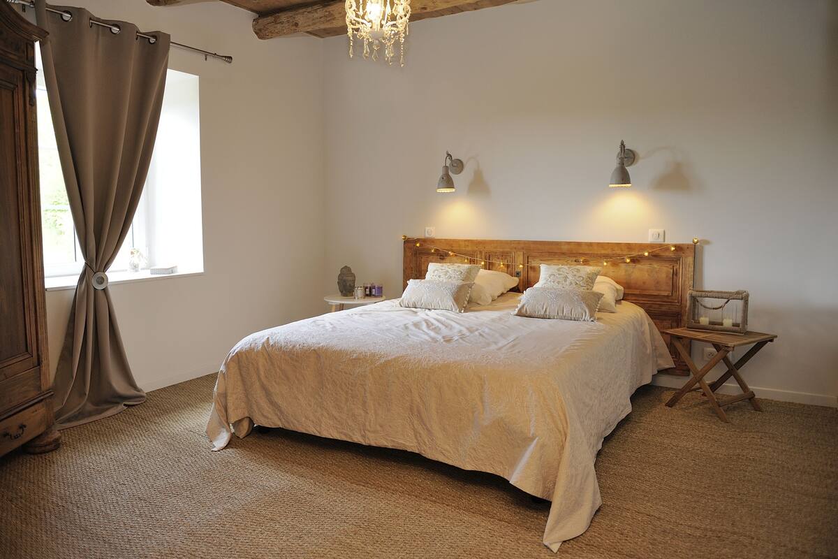 A bedroom with a large bed, wooden headboard, bedside lamps, and a window with curtains.