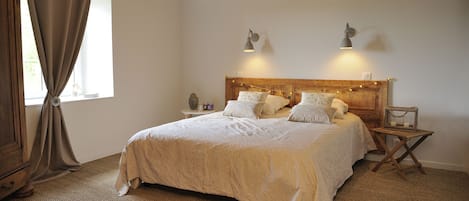 A bedroom with a large bed, wooden headboard, bedside lamps, and a window with curtains.