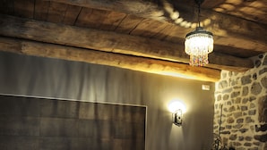 A modern bathroom with a large bathtub, a stone wall, and a hanging light fixture. - B&B Au Chant De L'eau (Siaugues-Sainte-Marie)