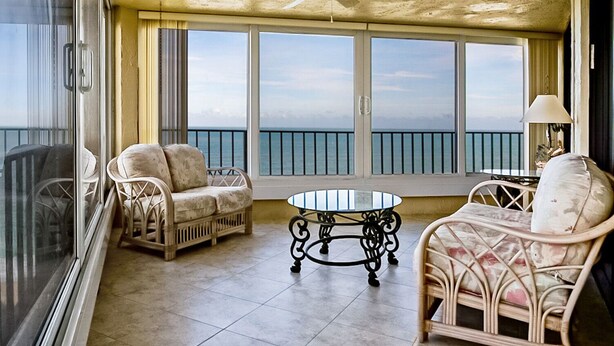 A balcony with wicker furniture, a glass table, and a view of the ocean. - SS 81122 Expansive Ocean & Intracoastal Waterway View Condo - Vacation Rental in Ocean Village (Fort Pierce)