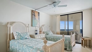 A bedroom with two beds, a ceiling fan, a painting, and a view of the ocean. - SS 81122 Expansive Ocean & Intracoastal Waterway View Condo - Vacation Rental in Ocean Village (Fort Pierce)