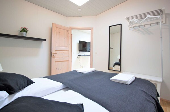 A bedroom with a bed, a wooden door, a mirror, a TV, and a drying rack.