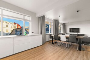 Una habitación de hotel moderna con un ventanal grande, un área de comedor con mesa y sillas, un televisor de pantalla plana y vistas a un edificio.