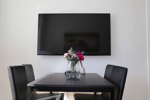 Una mesa de comedor con sillas, un jarrón con flores y un televisor de pantalla plana montado en la pared.
