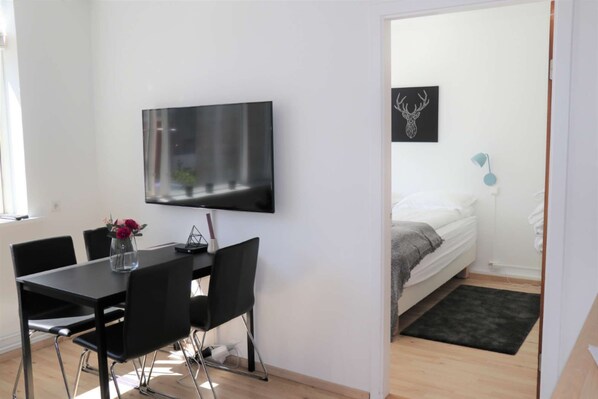 Una habitación moderna con una televisión de pantalla plana montada en la pared, una cama con una lámpara azul y una pequeña mesa con sillas.