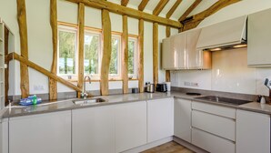 A modern kitchen with exposed wooden beams, a large window, and white cabinetry. - 1 bedroom accommodation in Raydon near Ipswich (Raydon near Ipswich)