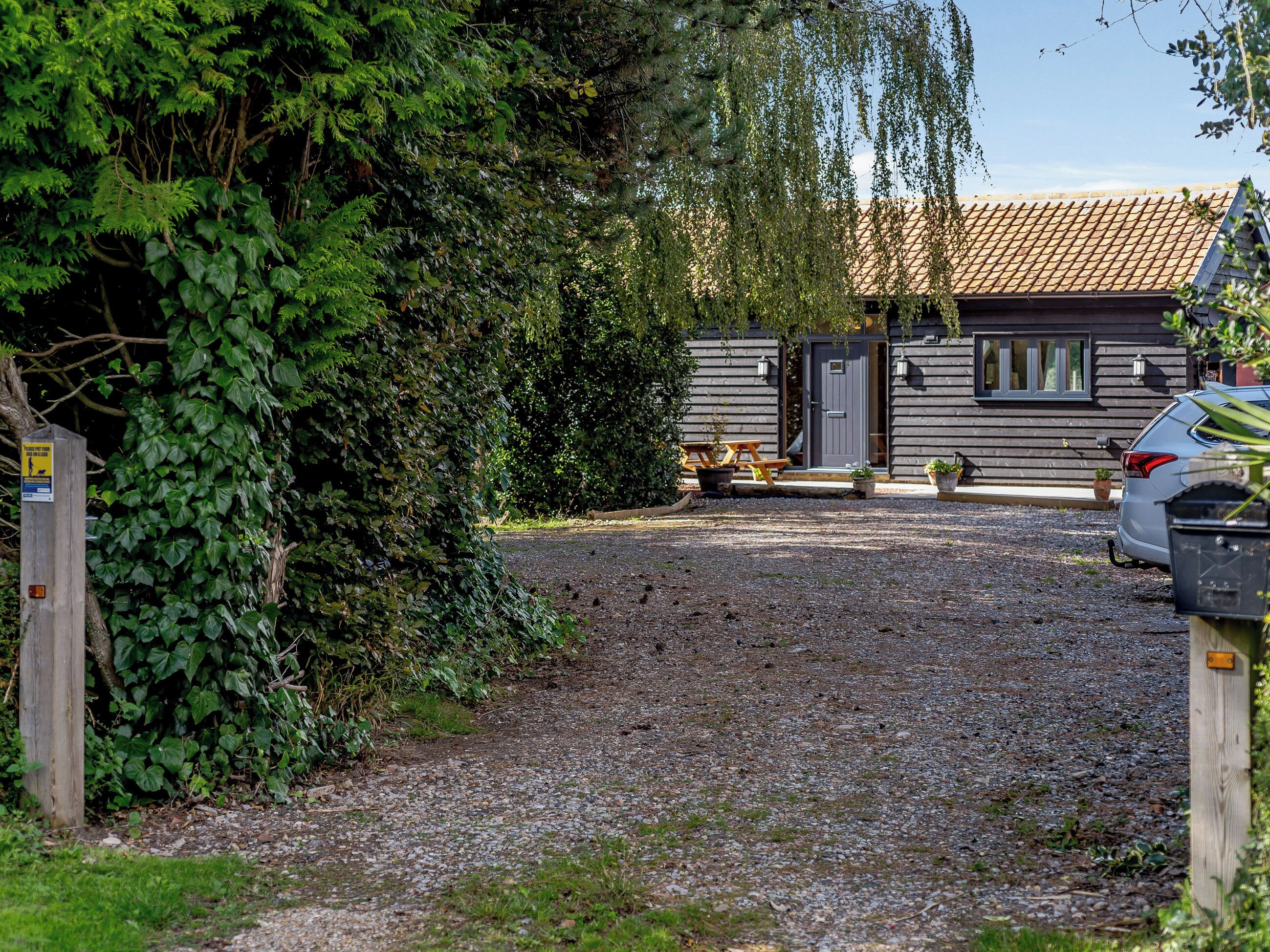 A gravel driveway leading to a wooden cabin with a tiled roof, surrounded by dense greenery.