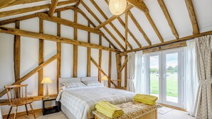 A bedroom with a bed, wooden headboard, bedside tables, a lamp, a chair, and a view of the outdoors through a glass door. - 1 bedroom accommodation in Raydon near Ipswich (Raydon near Ipswich)