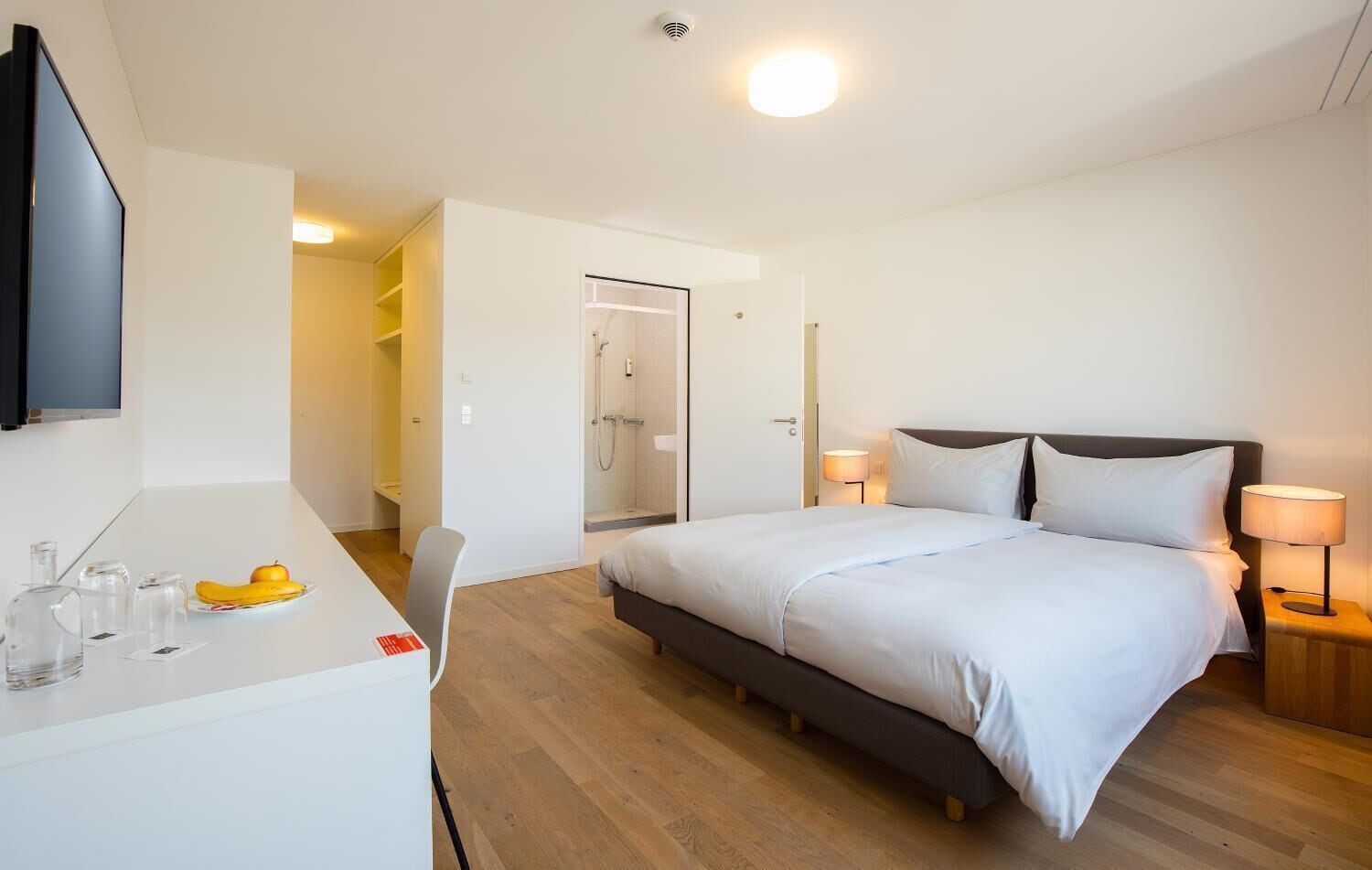 Een moderne hotelkamer met een bed, bedlampjes, een bureau met stoel en een douche.