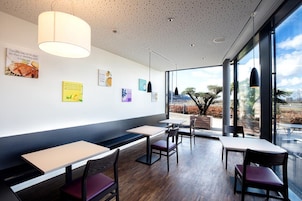 Interior moderno de restaurante con mesas y sillas de madera, un ventanal con vistas al exterior y varios carteles en la pared.
