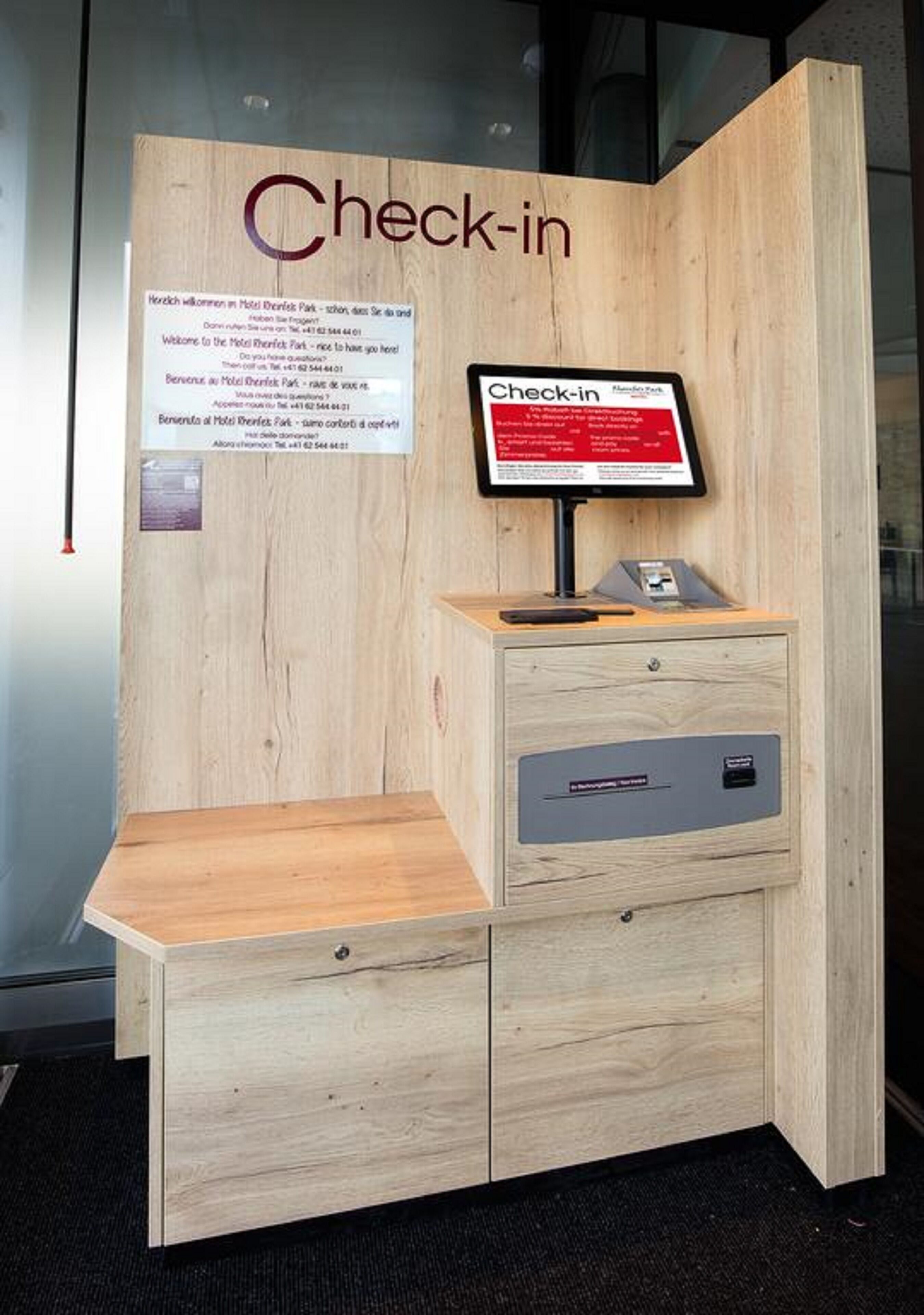 Un mostrador de recepción de madera con una pantalla digital y un pequeño escritorio.