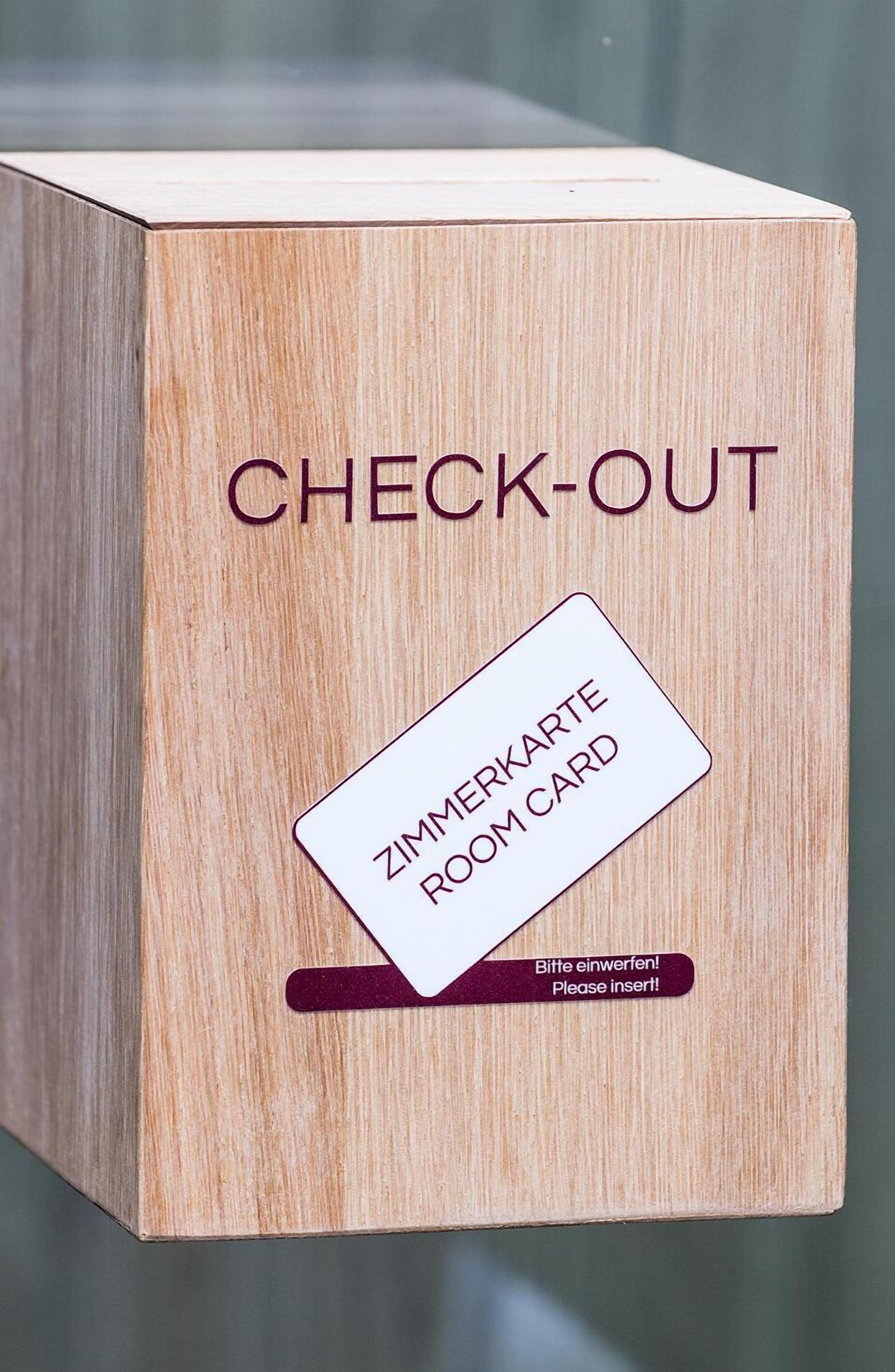 A wooden box labeled "CHECK-OUT" with a "ROOM CARD" and a prompt to "Please insert!"