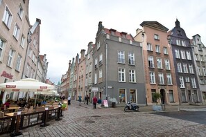 En kullerstensgata kantad av historiska byggnader, uteservering vid ett café och en parkerad motorcykel.
