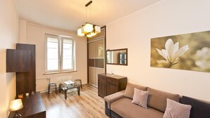 Un salon moderne avec un canapé, une table à manger et une table basse. Il y a une fenêtre avec des stores, un miroir et un tableau encadré au mur.
