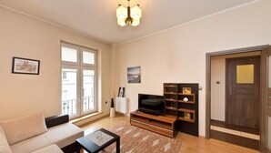 Un salon avec un canapé, une table basse, un téléviseur posé sur un meuble en bois et une porte sur le côté droit.