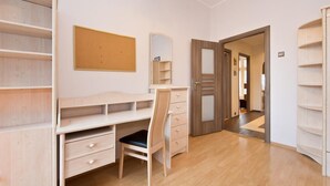 Une chambre à coucher avec un bureau en bois, une chaise, une armoire et une porte donnant sur une autre pièce.