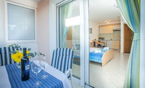 A hotel room with a bed, a dining area with a table and chairs, a kitchen visible through an open door, and a balcony with a table and chairs. -  Ground-floor studio for 3, 🏝 beach at 50 m, Seget (Seget Donji)