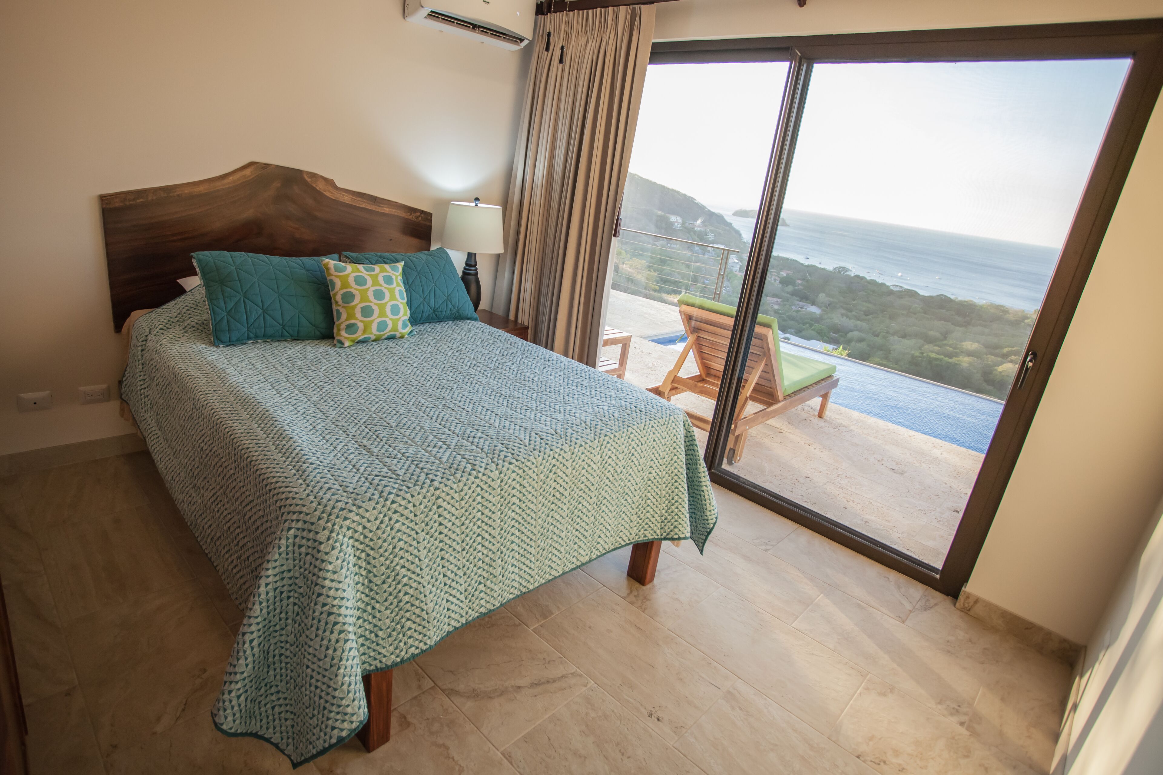 Un dormitorio con una cama grande, vista al mar a trav és de una puerta corrediza de vidrio y un balcón con una silla.