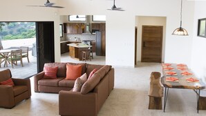 A spacious living area with a brown sofa, a dining table with placemats, and a kitchen in the background. - Casa de la Paz (Sardinal)