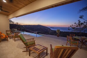 A wooden deck with outdoor furniture, a pool, and a view of the ocean at dusk. - Casa de la Paz (Sardinal)