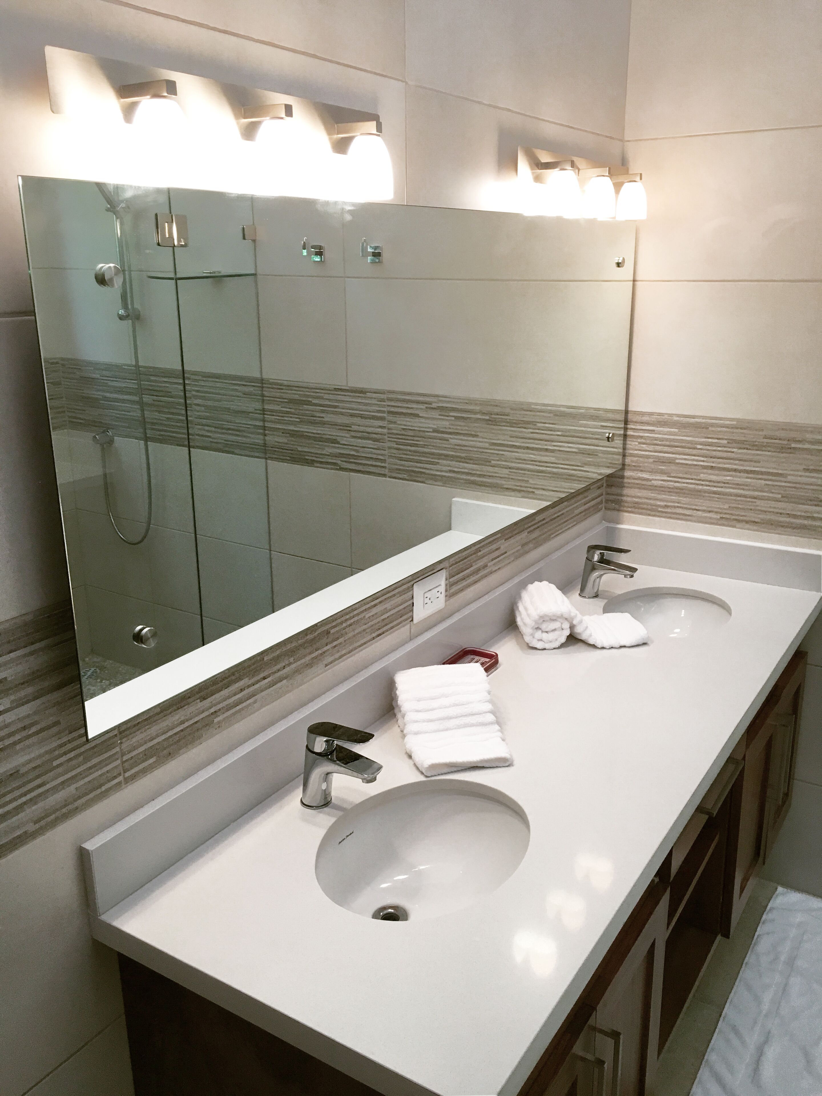 A modern bathroom with two sinks, a large mirror, and a glass shower enclosure.