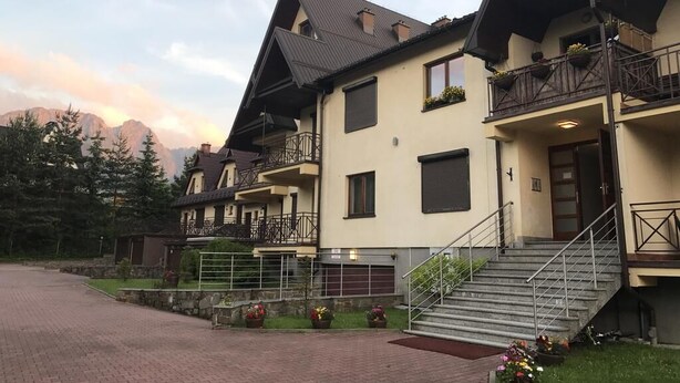 Eine Reihe von Chalets mit Balkonen, eine gepflasterte Auffahrt und ein Berg im Hintergrund.