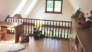 Ein Zimmer mit Holztisch, einer Couch, einem Panda-Plüschtier, einem Fenster und einer Chandelier.